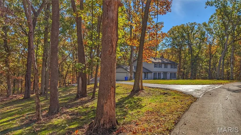 Two-story residence featuring a light-colored exterior, attached garage, paved driveway, and substantial wooded lot — 1444 Eagle Ridge Road, Wildwood, MO 63038