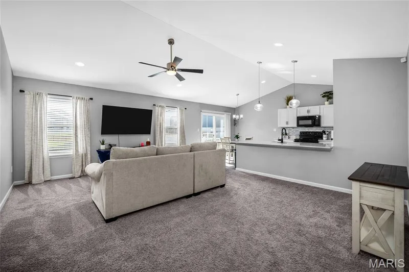 Vaulted ceiling with recessed lighting and a ceiling fan, gray carpeting, kitchen pass-through with pendant lighting, and white cabinetry — 302 Creek Sound Court, Wentzville, MO 63385