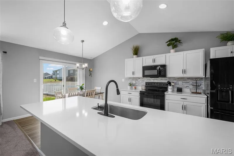 Kitchen featuring a large central island with an undermount sink, white cabinetry, black appliances, and a tile backsplash — 302 Creek Sound Court, Wentzville, MO 63385