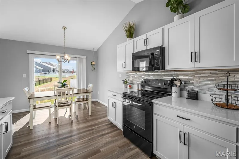 Kitchen featuring white cabinetry, black appliances, light-toned countertops, a glass tile backsplash, and wood-finish flooring — 302 Creek Sound Court, Wentzville, MO 63385