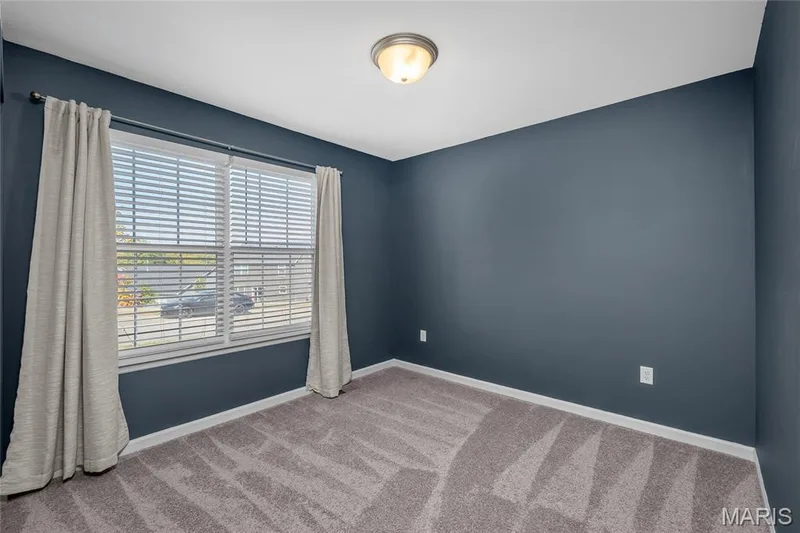 Wall-to-wall carpeting with geometric pattern, white trim, window with blinds, and flush mount ceiling light — 302 Creek Sound Court, Wentzville, MO 63385