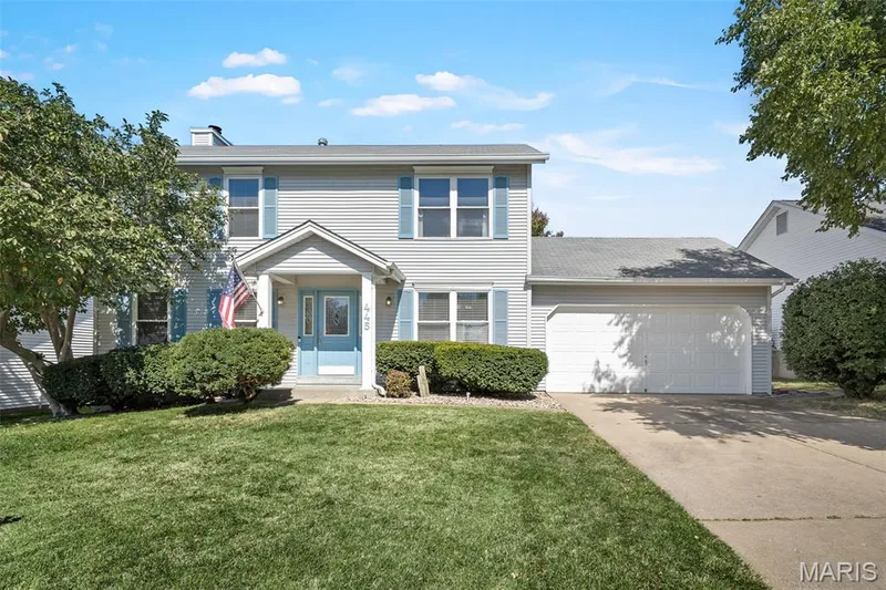 Two-story residence featuring light gray siding, blue window shutters, an attached two-car garage, concrete driveway, and a covered entryway — 445 Lantana Lane, St Peters, MO 63376