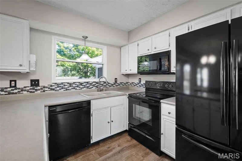 White cabinetry, stainless steel sink with gooseneck faucet, black appliances, and mosaic tile backsplash — 445 Lantana Lane, St Peters, MO 63376