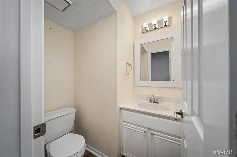 White vanity with integrated sink, chrome faucet, wall-mounted mirror with textured frame, and a three-light vanity fixture — 445 Lantana Lane, St Peters, MO 63376