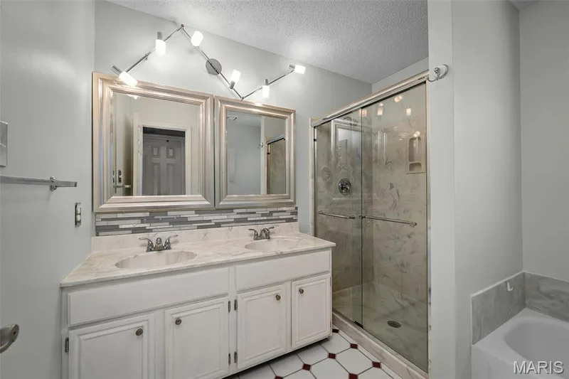 Dual vanity with integrated sinks, framed mirrors, glass-enclosed shower, mosaic tile backsplash, and patterned floor tiles — 445 Lantana Lane, St Peters, MO 63376