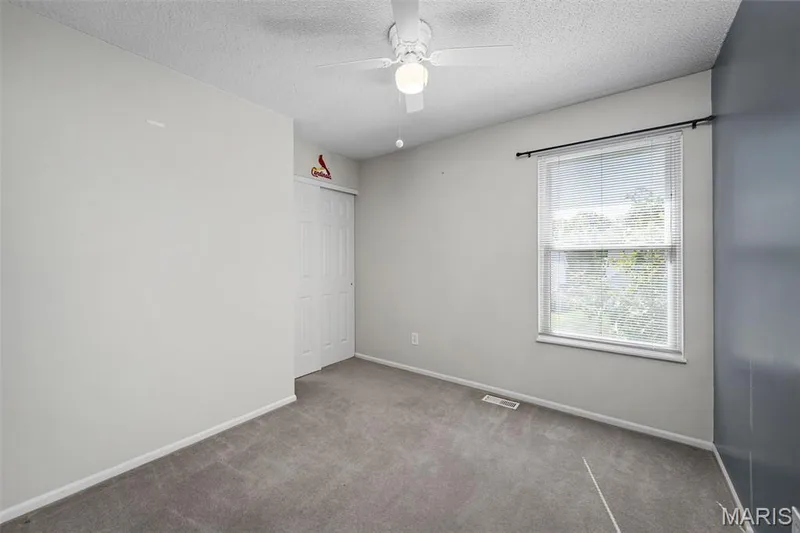 Neutral wall paint, ceiling fan with integrated lighting, window with blinds, bi-fold closet doors, and gray carpet flooring — 445 Lantana Lane, St Peters, MO 63376