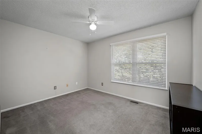 Carpeted room with a ceiling fan, a large window featuring blinds, and light-toned walls — 445 Lantana Lane, St Peters, MO 63376
