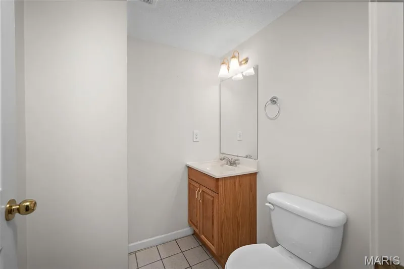 Wood-finish vanity with a light-toned countertop, integrated sink, and wall-mounted mirror — 445 Lantana Lane, St Peters, MO 63376