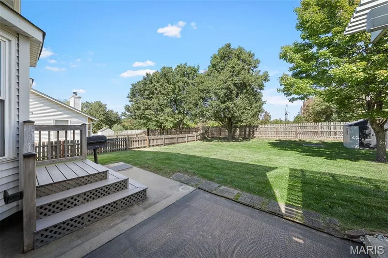 Expansive fenced backyard featuring a wood deck with steps, a concrete patio, and a storage shed — 445 Lantana Lane, St Peters, MO 63376