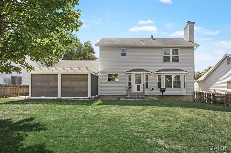 Expansive backyard with a manicured lawn, an attached pergola structure featuring two screened sections, and a bay window on the home's exterior — 445 Lantana Lane, St Peters, MO 63376