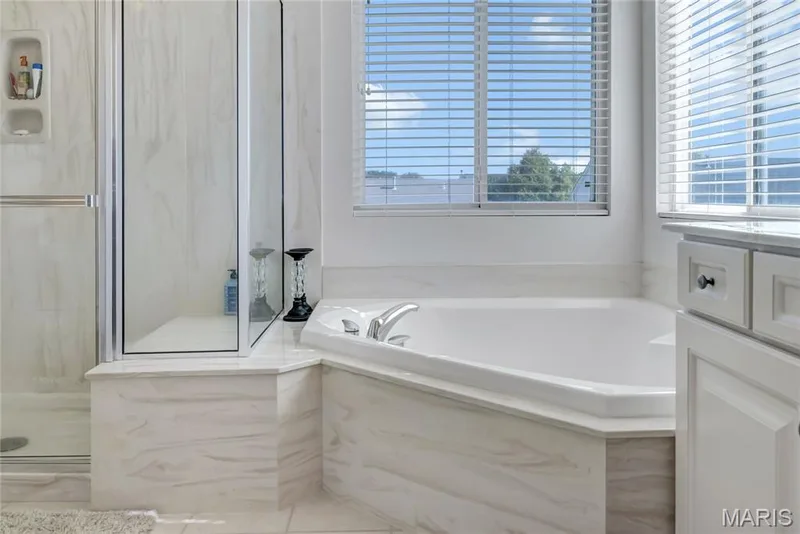 Corner soaking tub with integrated surround, glass-enclosed shower, light-toned cabinetry, and horizontal window blinds — 2061 Avalon Mist Circle, Dardenne Prairie, MO 63368
