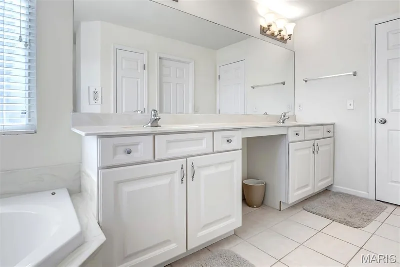 Dual vanity featuring white shaker-style cabinetry, solid-surface countertops, integrated sinks, a full-width vanity mirror, and three-light decorative wall fixture — 2061 Avalon Mist Circle, Dardenne Prairie, MO 63368