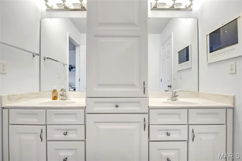 Double vanity featuring white cabinetry, a central storage tower, light-toned stone-finish countertops, undermount sinks, and chrome fixtures — 2061 Avalon Mist Circle, Dardenne Prairie, MO 63368