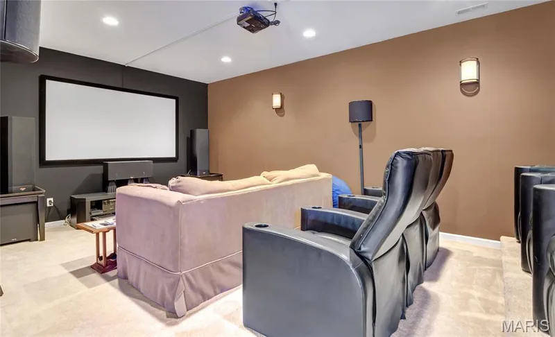 Media room featuring a fixed projector screen, recessed ceiling lighting, wall-mounted light fixtures, and a tiered platform floor — 2061 Avalon Mist Circle, Dardenne Prairie, MO 63368