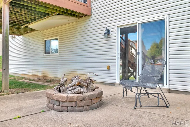 Concrete patio featuring a circular stone fire pit, siding exterior, sliding glass door, and overhead wooden deck structure — 2061 Avalon Mist Circle, Dardenne Prairie, MO 63368