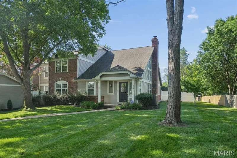 Two-story residence featuring brick and siding facade, covered front entry, arched window, a prominent brick chimney, and mature trees — 15826 Harris Ridge Court #15826, Chesterfield, MO 63017