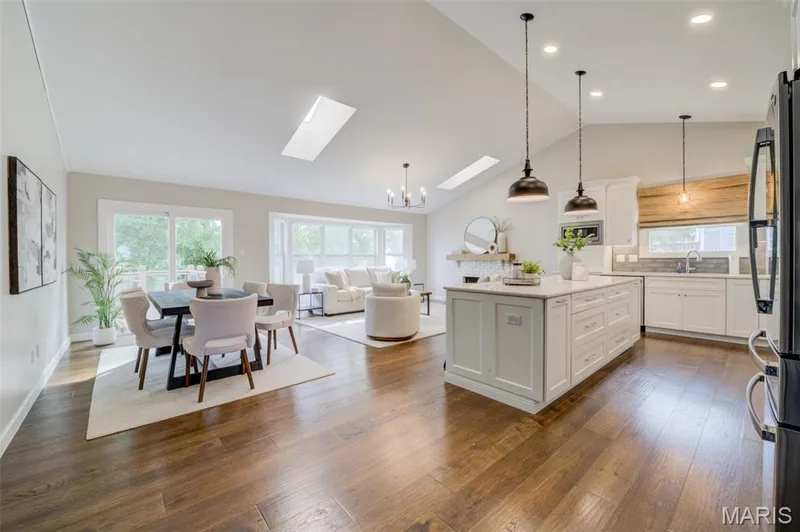 Vaulted ceilings with skylights, wood-finish flooring, white kitchen cabinetry, a kitchen island, and sliding glass doors — 1094 Harness Drive, St Charles, MO 63304