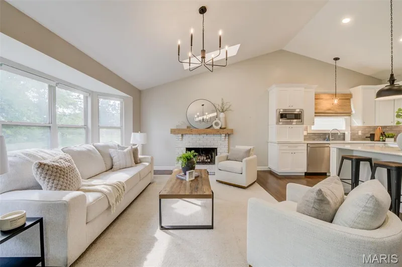 Vaulted ceiling with an open-concept layout, bay window, white brick fireplace, and kitchen with white cabinetry and stainless steel appliances — 1094 Harness Drive, St Charles, MO 63304