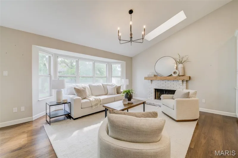 Vaulted ceiling with a skylight, white brick fireplace with a wood mantle, bay window, dark wood-finish flooring, and a modern chandelier — 1094 Harness Drive, St Charles, MO 63304