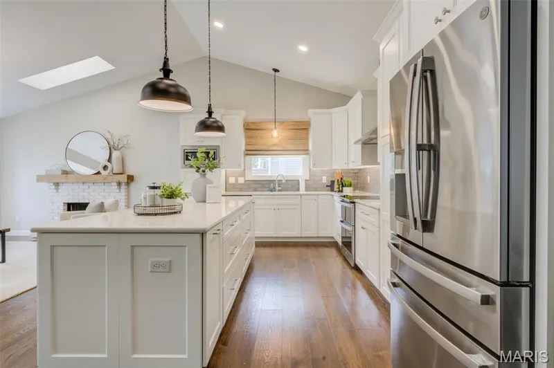 Vaulted ceiling with skylight, extensive wood-finish flooring, white shaker cabinetry, stainless steel appliances, and a quartz-surfaced island — 1094 Harness Drive, St Charles, MO 63304