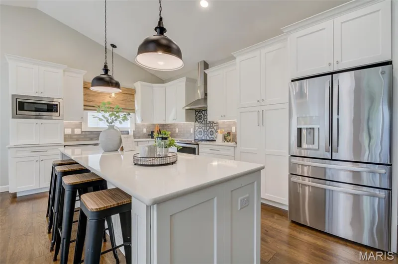 Kitchen featuring vaulted ceilings, white cabinetry, stainless steel appliances, a center island with countertop seating, and wood-finish flooring — 1094 Harness Drive, St Charles, MO 63304
