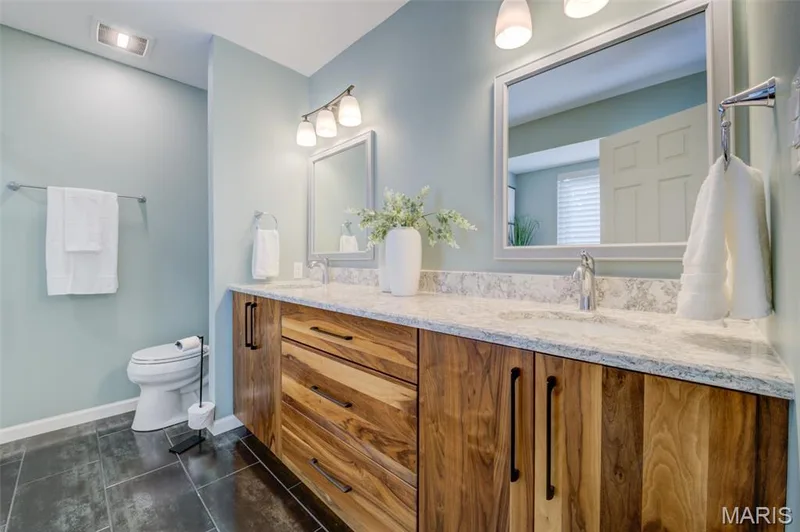 Dual vanity with wood-finish cabinetry, light-toned countertop, and dual framed mirrors — 1094 Harness Drive, St Charles, MO 63304