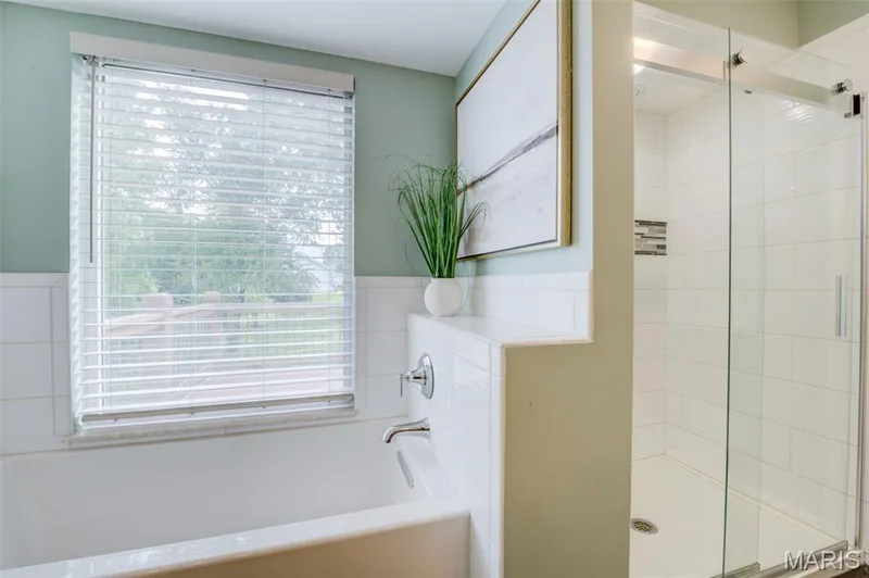 Soaking tub with a polished chrome faucet, white tile surround, and a window with horizontal blinds — 1094 Harness Drive, St Charles, MO 63304