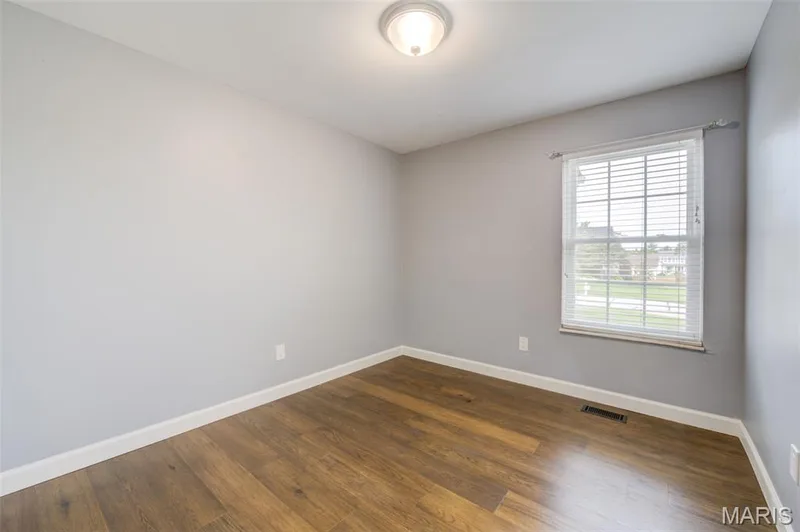 Neutral painted walls, wood-finish flooring, white trim, and a window with blinds — 1094 Harness Drive, St Charles, MO 63304