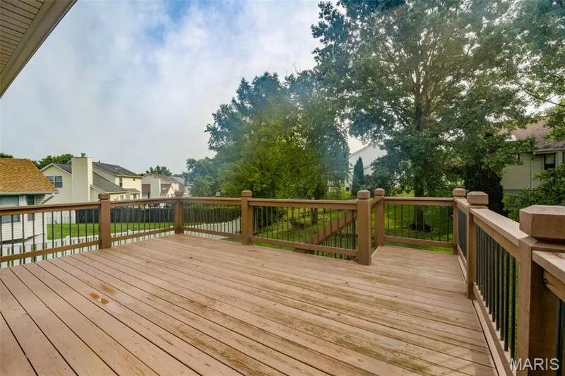 Expansive outdoor deck with wood-finish decking and dark balusters, surrounded by mature trees — 1094 Harness Drive, St Charles, MO 63304