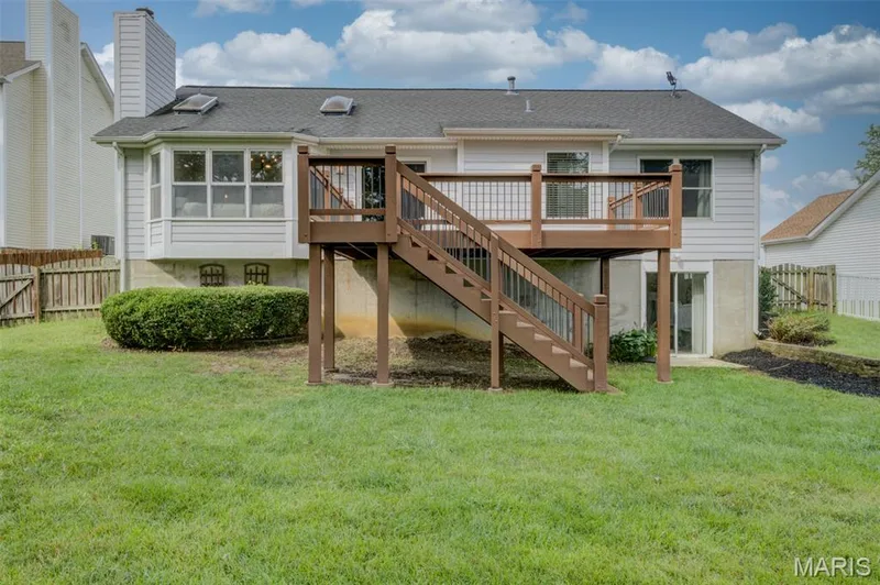 Expansive green lawn, elevated wood-finish deck with railings and stairs, bay window, sliding glass door access, and skylights — 1094 Harness Drive, St Charles, MO 63304