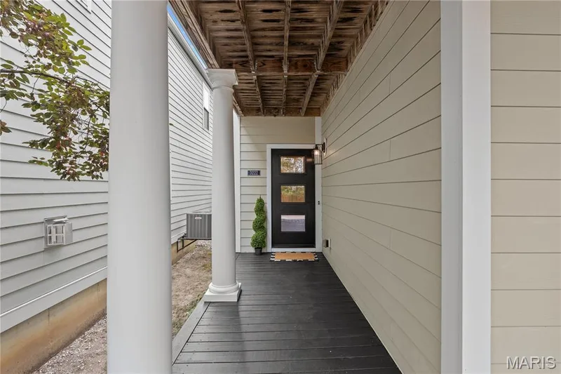 Covered entryway featuring horizontal lap siding, structural columns, exposed wood-joist ceiling, and a multi-pane front door with a matte-finish exterior lantern fixture — 3222 Starkville Street, St Charles, MO 63301