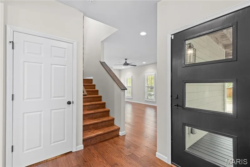 Foyer featuring a black three-panel front door with glass inserts, wood-finish flooring, and a staircase with a wood-finish tread design — 3222 Starkville Street, St Charles, MO 63301