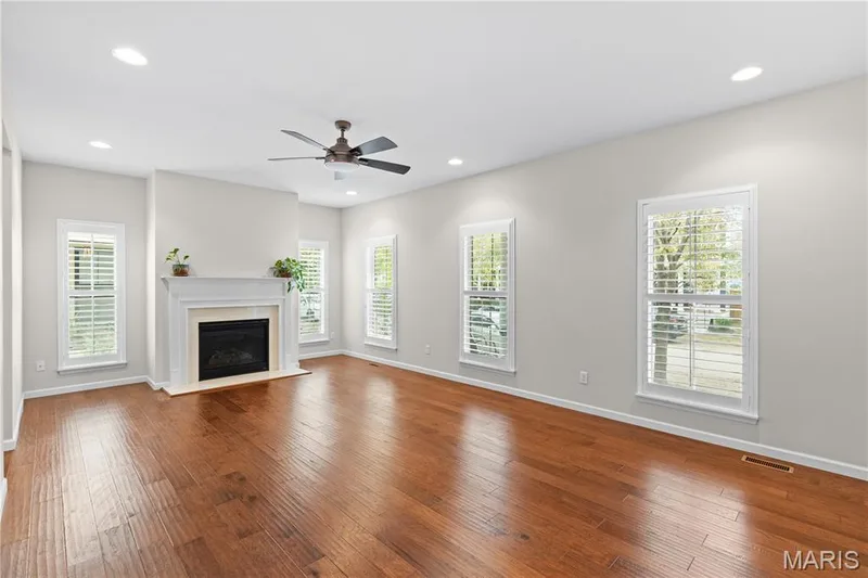 Living area featuring wood-finish flooring, a fireplace with a decorative mantel, recessed lighting, a ceiling fan, and windows with interior plantation shutters — 3222 Starkville Street, St Charles, MO 63301