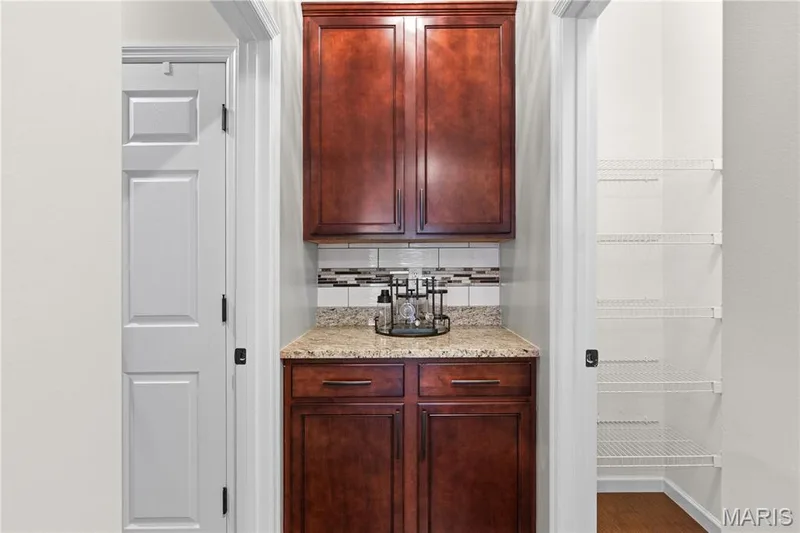 Built-in cabinetry featuring dark wood-finish, stone-finish countertop, decorative tile backsplash, and integrated wire shelving storage — 3222 Starkville Street, St Charles, MO 63301
