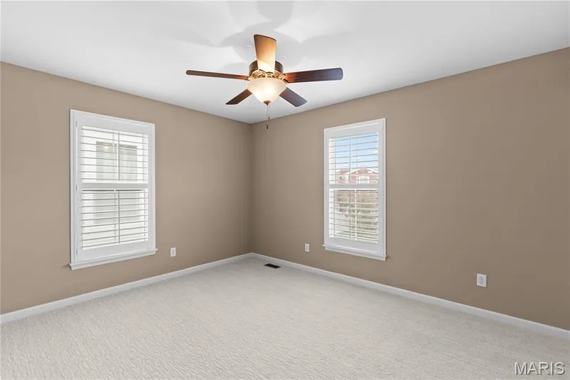 Room featuring neutral wall tones, wall-to-wall carpeting, dual windows with interior shutters, and a ceiling fan with integrated lighting — 3222 Starkville Street, St Charles, MO 63301