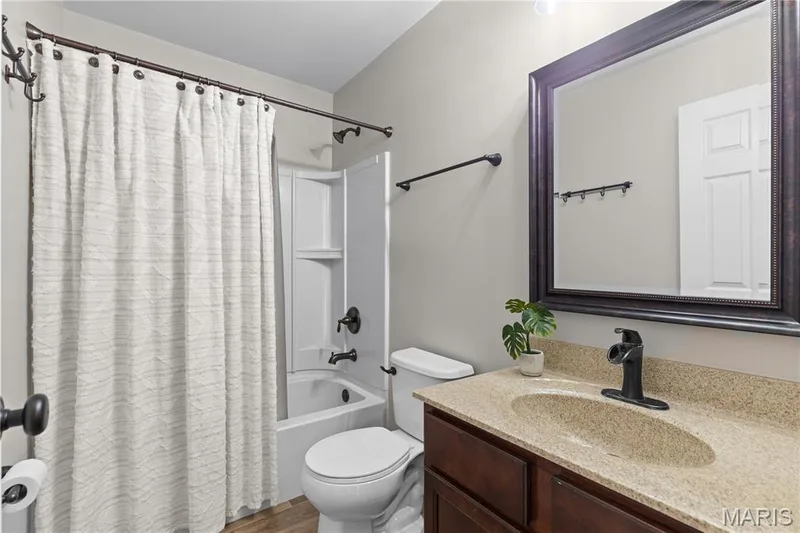 Bathroom featuring a dark wood vanity with a stone-finish countertop, oval undermount sink, oil-rubbed bronze fixtures, and a tub-shower combination with integrated shelving — 3222 Starkville Street, St Charles, MO 63301