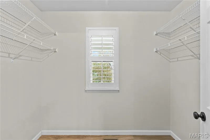 Walk-in closet featuring white wire shelving, a centered window with plantation shutters, and wood-finish flooring — 3222 Starkville Street, St Charles, MO 63301