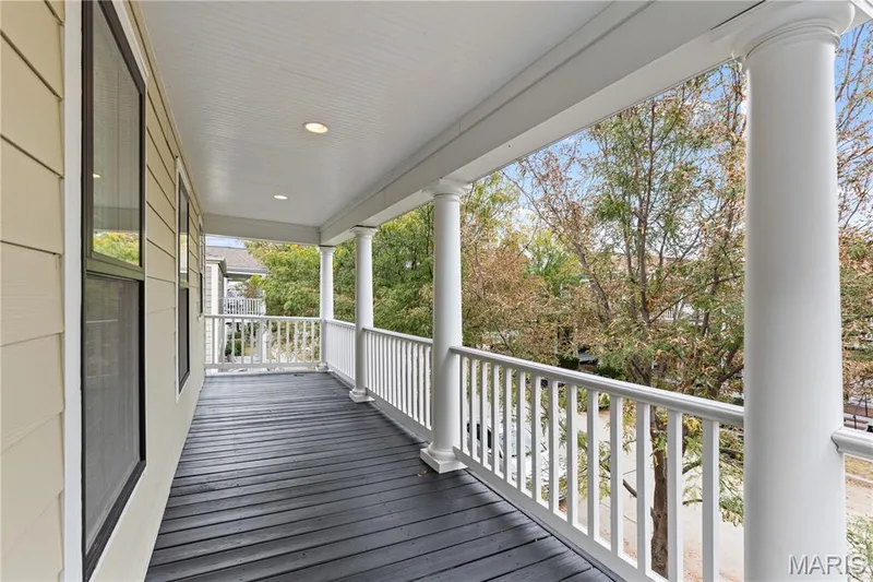 Covered balcony featuring dark-stained wood-finish flooring, white structural columns, recessed lighting, and a white rail balustrade — 3222 Starkville Street, St Charles, MO 63301