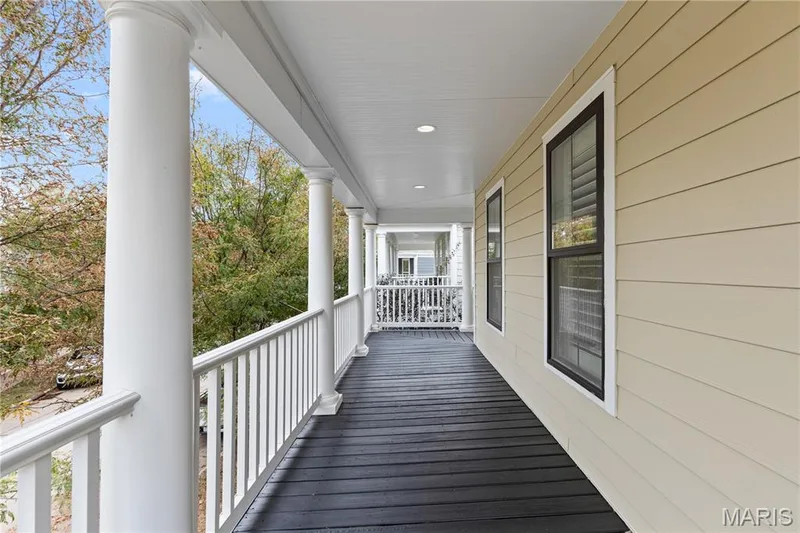 Covered porch featuring dark wood-finish decking, crisp white balusters, classic round columns, and recessed lighting — 3222 Starkville Street, St Charles, MO 63301