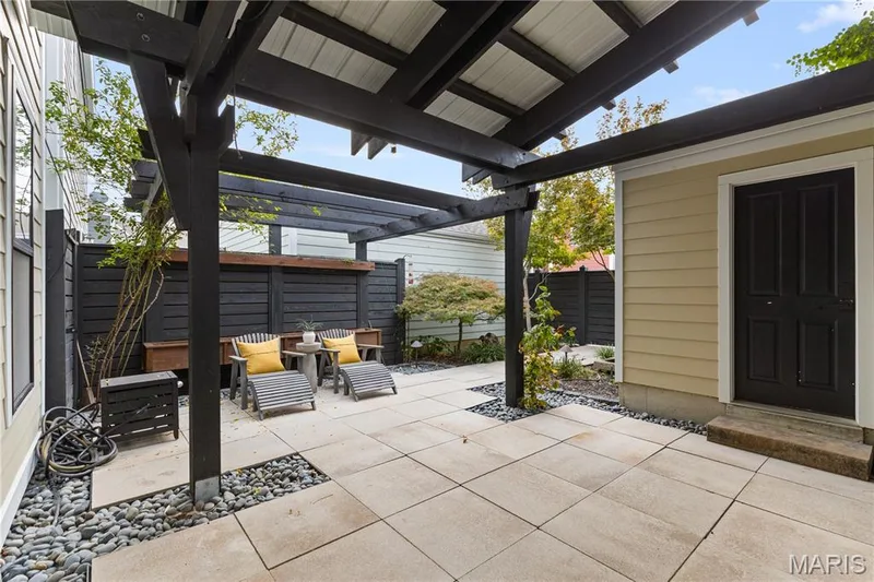 Outdoor living space featuring a structured timber pergola, concrete tile patio, decorative stone accents, and enclosed perimeter fencing — 3222 Starkville Street, St Charles, MO 63301