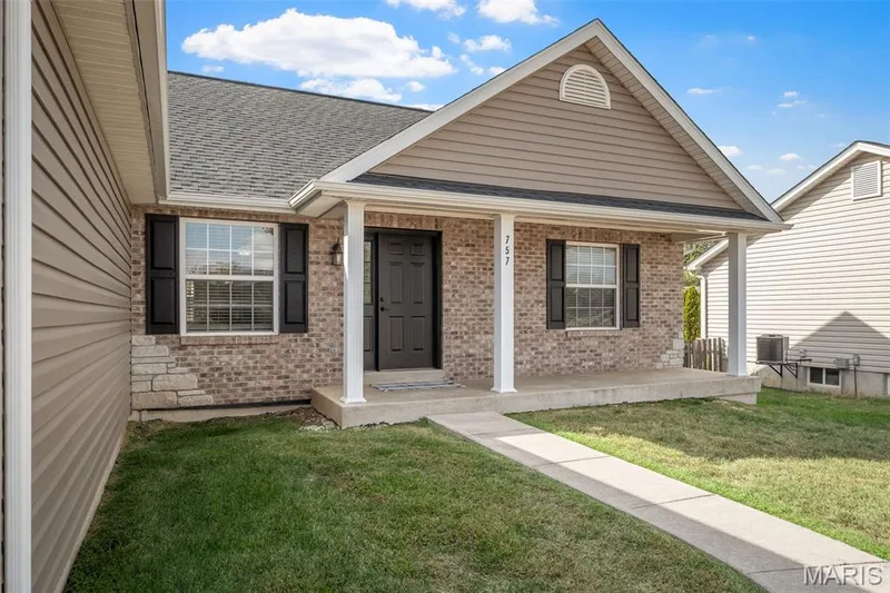 Exterior facade featuring a brick and vinyl siding finish, covered front porch, arched accent window, and dark shutter trim — 757 Lost Canyon Boulevard, Wentzville, MO 63385