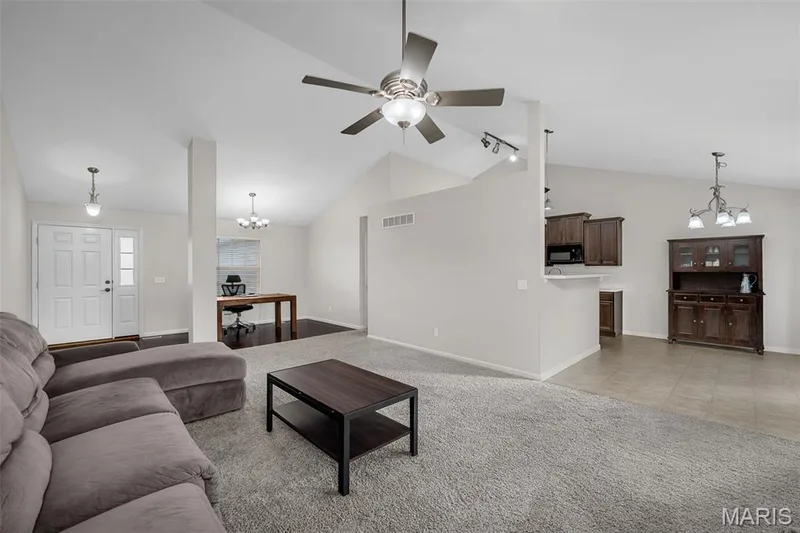 Open-concept living space featuring vaulted ceilings, a central ceiling fan with integrated lighting, neutral carpet flooring, and multi-light chandeliers — 757 Lost Canyon Boulevard, Wentzville, MO 63385