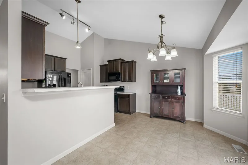 Kitchen featuring dark wood cabinetry, a raised breakfast bar with a solid surface countertop, neutral flooring, a vaulted ceiling, and tiered chandelier lighting — 757 Lost Canyon Boulevard, Wentzville, MO 63385