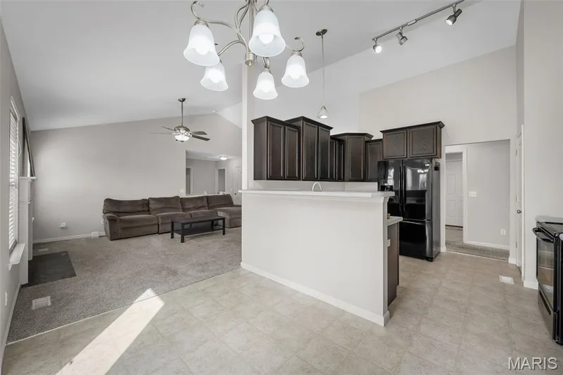 Vaulted ceilings featuring a multi-arm chandelier, dark-finish cabinetry, breakfast bar, track lighting, and built-in appliances — 757 Lost Canyon Boulevard, Wentzville, MO 63385