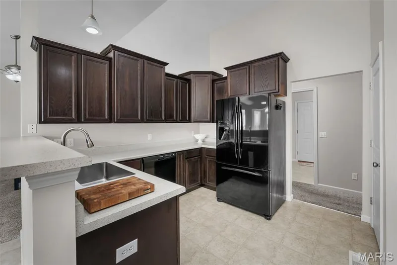 Kitchen featuring dark-finish cabinetry, light-toned solid surface countertops, stainless steel undermount sink, black appliances, and vaulted ceilings — 757 Lost Canyon Boulevard, Wentzville, MO 63385