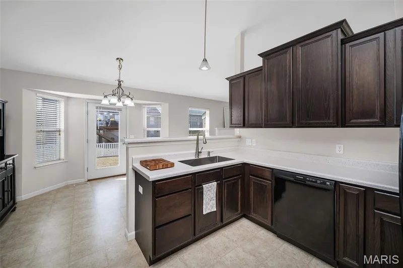 Kitchen featuring dark wood cabinetry, solid surface countertops, stainless steel undermount sink with a gooseneck faucet, black dishwasher, and neutral flooring — 757 Lost Canyon Boulevard, Wentzville, MO 63385