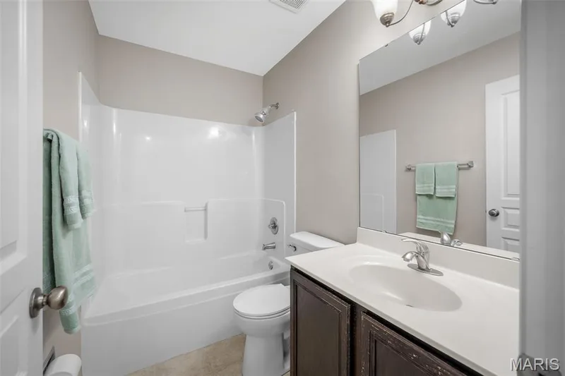 Hall Bathroom featuring a single-sink vanity with a solid-surface countertop, dark wood-finish cabinetry, a full-width wall mirror, and a white acrylic tub-and-shower surround with chrome fixtures — 757 Lost Canyon Boulevard, Wentzville, MO 63385
