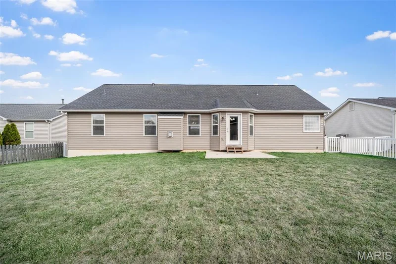 Rear exterior featuring beige horizontal siding, asphalt shingle roofing, a concrete patio, and a fenced backyard — 757 Lost Canyon Boulevard, Wentzville, MO 63385
