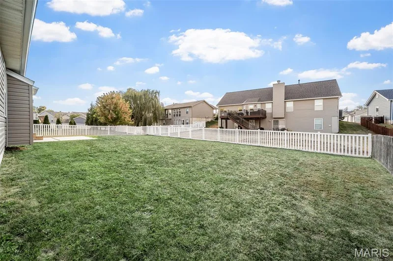 Expansive backyard featuring a level lawn, white picket-style fencing, and a concrete patio slab — 757 Lost Canyon Boulevard, Wentzville, MO 63385