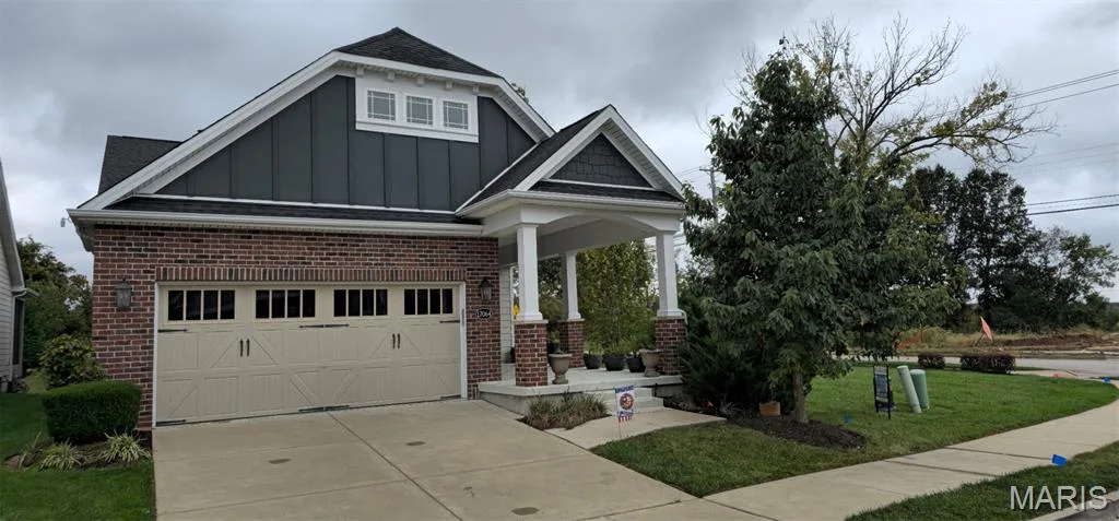 Brick exterior with vertical siding, covered front porch with square columns, and a multi-car garage featuring carriage-style doors — 17064 Fire Glow Drive, Wildwood, MO 63011